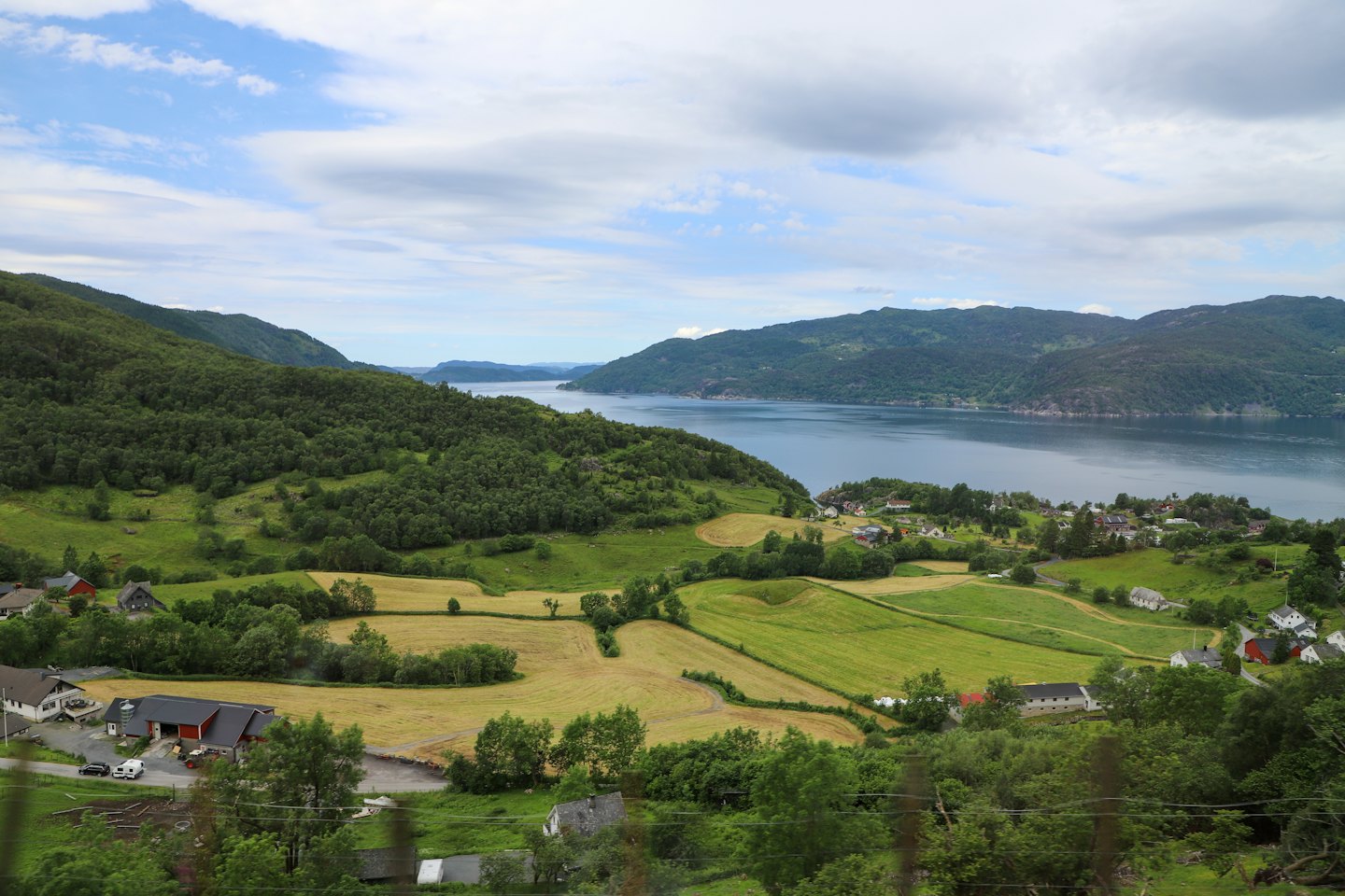 Tradisjonelle hus ligger langs en fjord mellom skogkledde fjellsider.